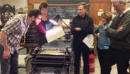 5 faculty and staff gather round old printing press