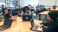three students work at table with laptops