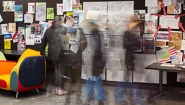 blurred by motion, students gather round bulletin board of hand-written opinions