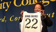Joanne Berger-Sweeney smiles and holds up Trinity athletic jersey with her last name and number 22 on it