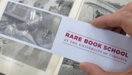 hand holding magnifier with logo for rare book school over old book