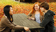 Tran, Altenhof-Long, and Peeler chat at picnic table with yellow leaves in background