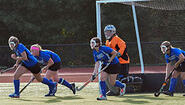 field hockey: goalie in net, four defenders running out