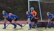 field hockey: goalie in net, four defenders running out