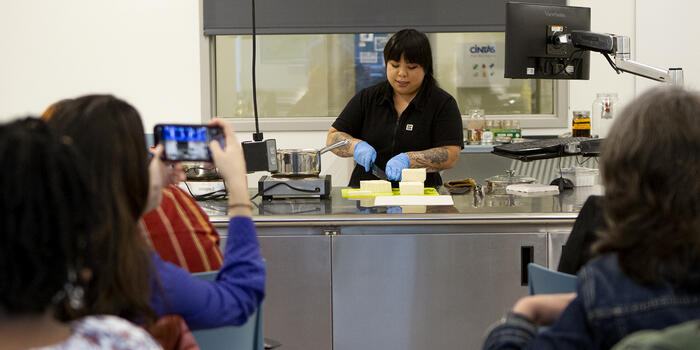 Bettina Makalintal ’14 cuts tofu in front of an audience in the cooking lab. 