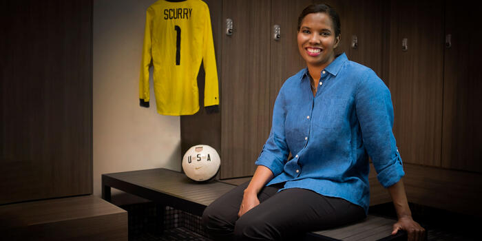 Briana Scurry posing on a bench with a soccer ball and jersey next to her