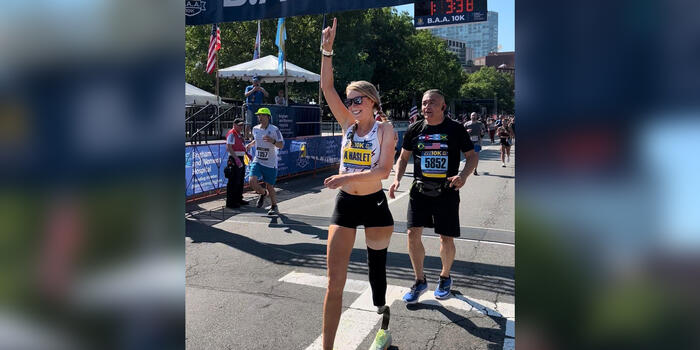Adrianne Haslet crosses a finish line, holding up her right hand in exaltation.
