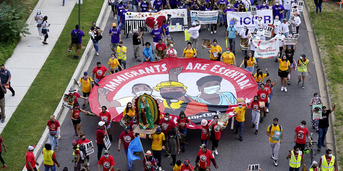 A bird's eye view of a protest march with a participants carrying a sign that says immigrants are essential workers.