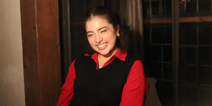 Lizette Ortega wears a long-sleeved red shirt and black sweater vest. She smiles at the camera.