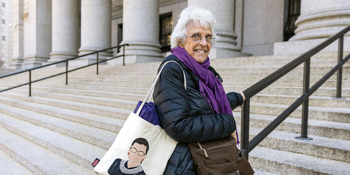 Nancy Stearns ’61 on the steps of the Thurgood Marshall U.S. Courthouse in New York City, holding a Ruth Bader Ginsburg tote bag