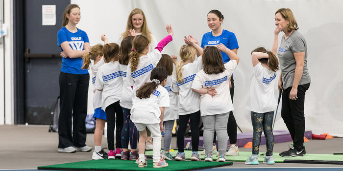 A group of young girls stand with Wellesley student athletes and a coach