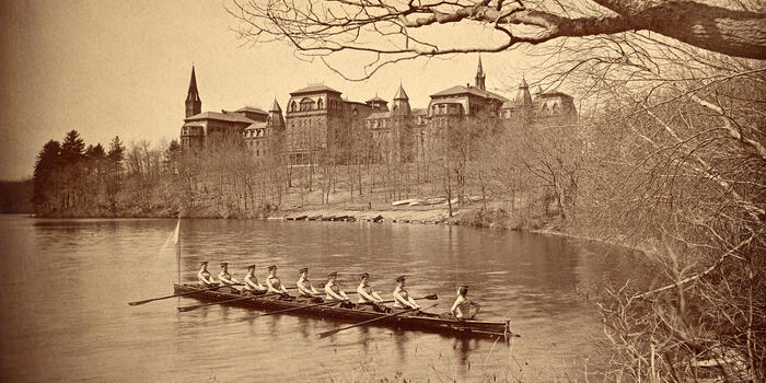 The class crew of 1894 rows on Lake Waban, with College Hall in the background.