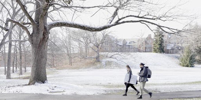 Two students walk across a snowy campus.