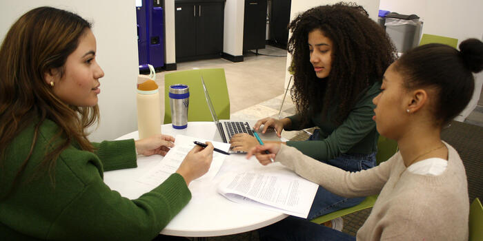 Three students sit at a table looking over papers.