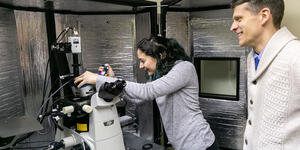 A student works with a microscope as a professor looks on