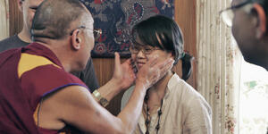 The Dalai Lama holds Amy Yee’s face in his hands as Yee laughs