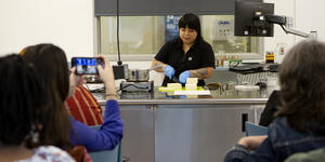 Bettina Makalintal ’14 cuts tofu in front of an audience in the cooking lab. 