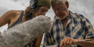 Cat Jaffee holds a microphone and leans toward a man holding a fishing net.