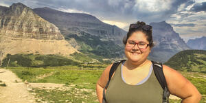 Photo of a woman looking at the camera smiling. There are mountains behind her.