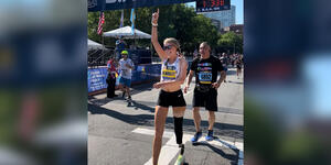 Adrianne Haslet crosses a finish line, holding up her right hand in exaltation.