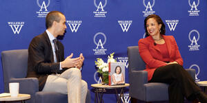 Susan Rice talks to a Wellesley professor in front of a blue backdrop 