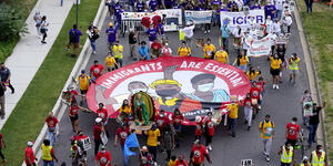 A bird's eye view of a protest march with a participants carrying a sign that says immigrants are essential workers.