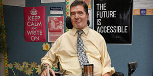 Jim Wice poses for a photo. Poster behind him reads The Future is Accessible.