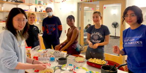 Students gather around a table where food is being made and they are smiling at the camera.