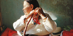 A photo of an older Hispanic woman braiding her long hair. 