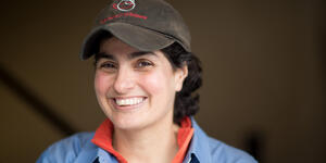 Portrait of alum Nergis Mavalvala wearing a cap and smiling at the camera.