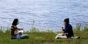 two students sitting by the lake reading books and talking