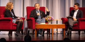 Haruki Murakami seated on stage and holding a microphone to answer a question.