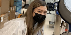 Kathryn Cross in a lab coat and black face mask looks at camera.