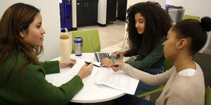 Three students sit at a table looking over papers.