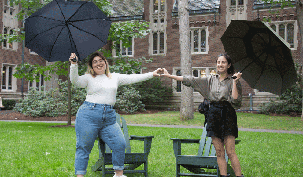 Two students stand by Adirondack chairs in the academic quad.