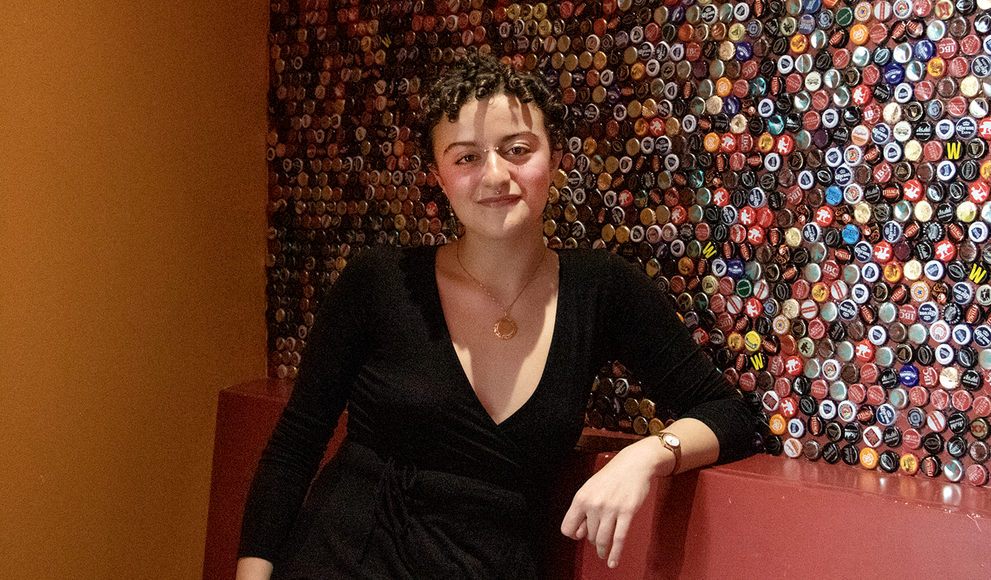 Aysar Abdelgelil poses next to a wall covered in bottle caps that is located in Punch's Alley.