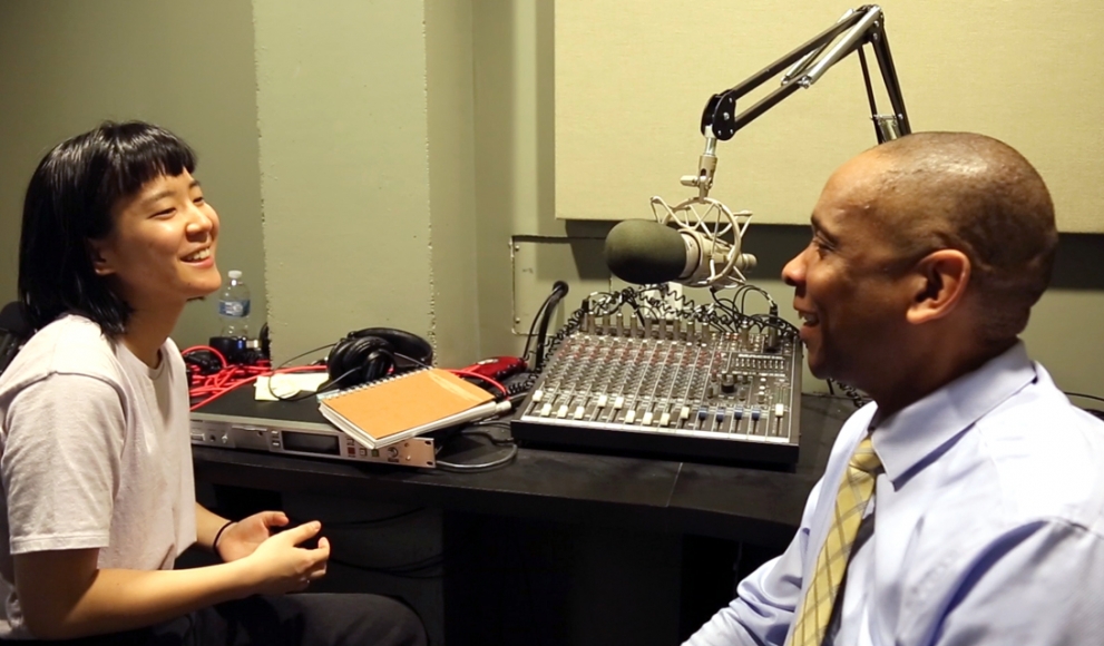 A student and staff member sit in a recording studio, talking. 