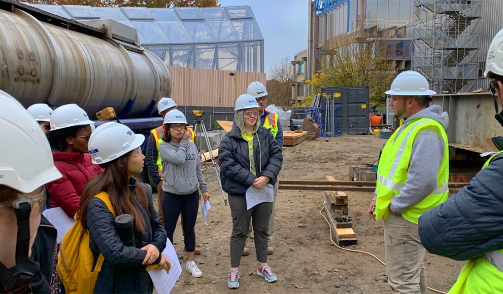 Students stand outside the science building wearing construction hats