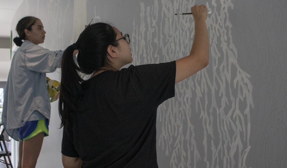 Two students work on a walled mural.