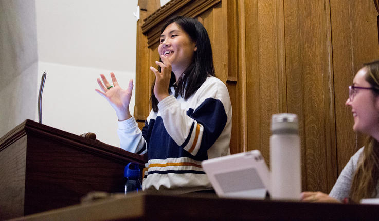 Diana Lam stands behind a lectern and gestures with her hand during a student government meeting.