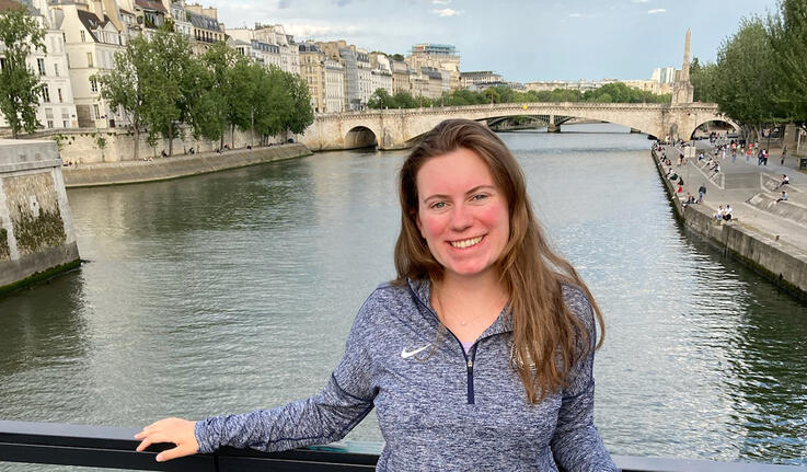 Rosalind Lucier ’22 stands in front of a channel of water with historic buildings behind her.