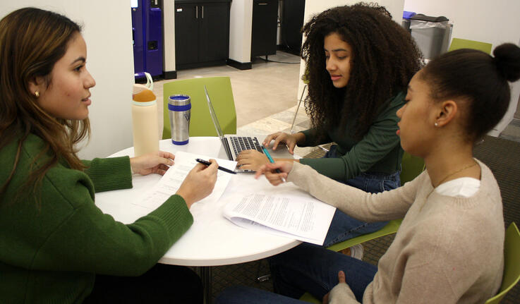 Three students sit at a table looking over papers.