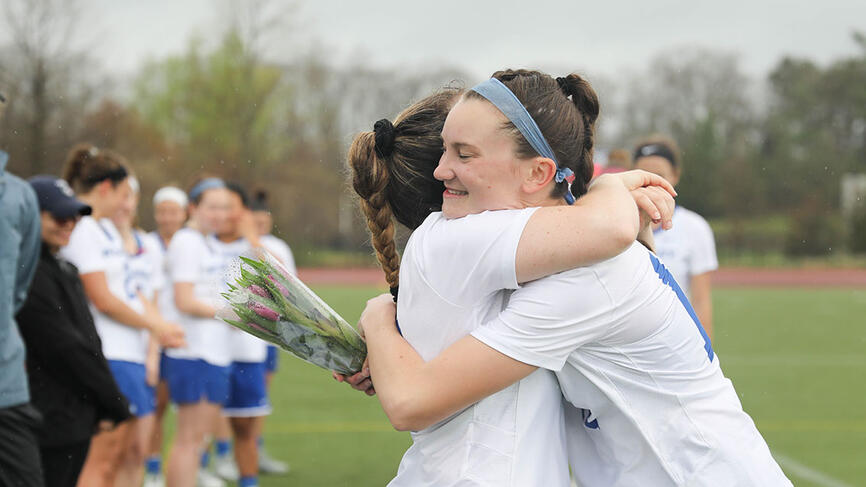 Two members of the lacrosse team hug on a field