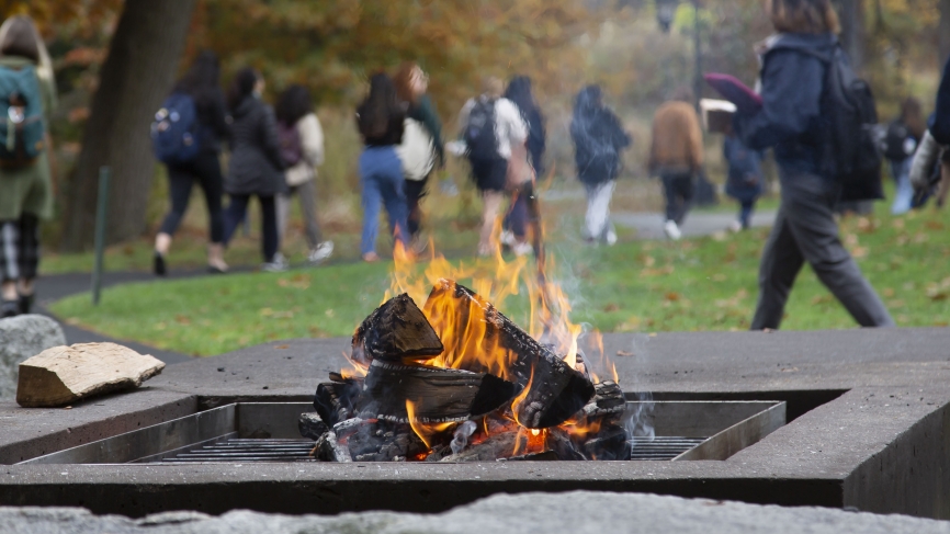 Students walk to lunch in Alumnae ballroom in the background. A fire pit is in the foreground. 