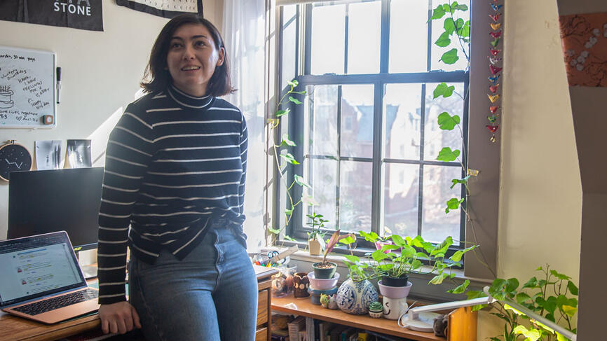 A student stands by her plants that sit in a window