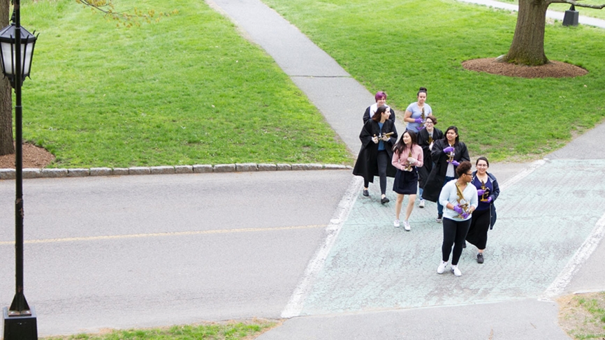 A group of students walk from the science complex to Green Hall holding the microscopes.