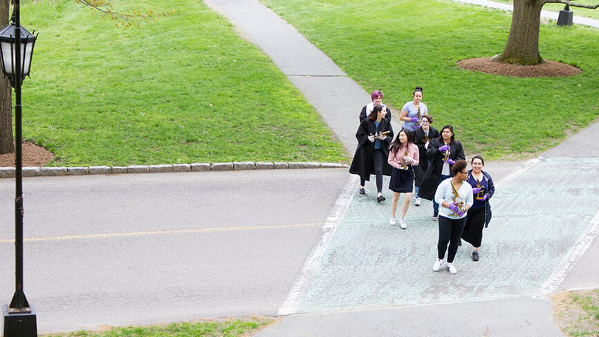 A group of students walk from the science complex to Green Hall holding the microscopes.