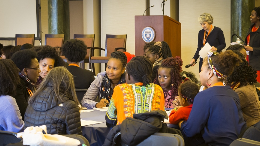 Groups of students sit at tables in deep discussion. 