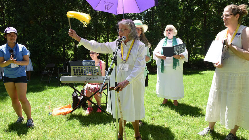An alumna from the class of 1939 stands outside, singing from a Wellesley song book.