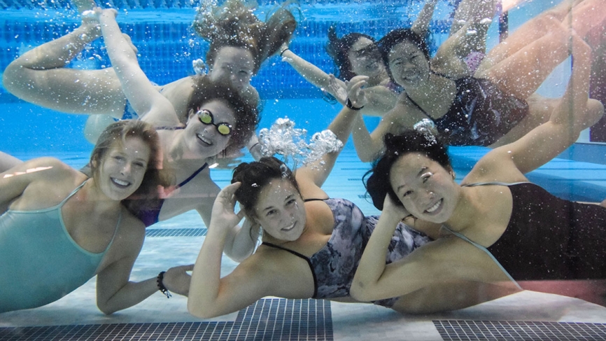 Swimmers pose underwater in a pool.